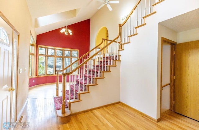 stairway with high vaulted ceiling, hardwood / wood-style floors, and ceiling fan with notable chandelier