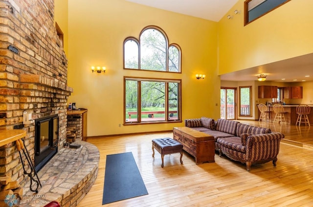 living room with brick wall, light hardwood / wood-style floors, a fireplace, and a towering ceiling