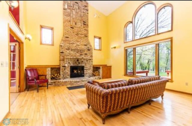 living room with a brick fireplace, high vaulted ceiling, and wood-type flooring