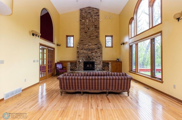 living room featuring brick wall, wood-type flooring, high vaulted ceiling, and a fireplace