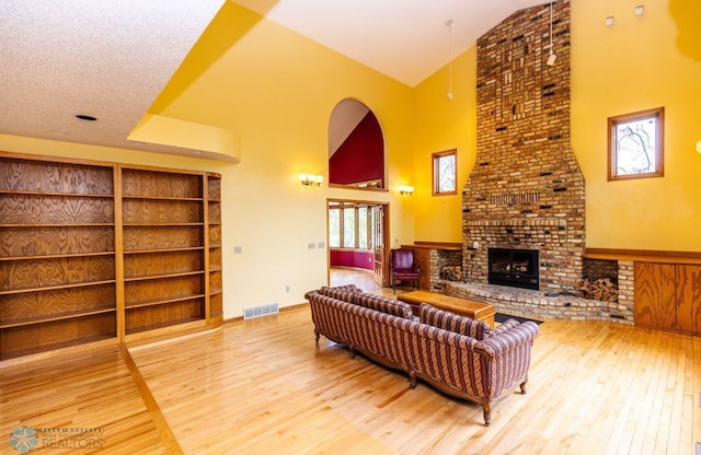 living room featuring a fireplace, wood-type flooring, a textured ceiling, brick wall, and high vaulted ceiling