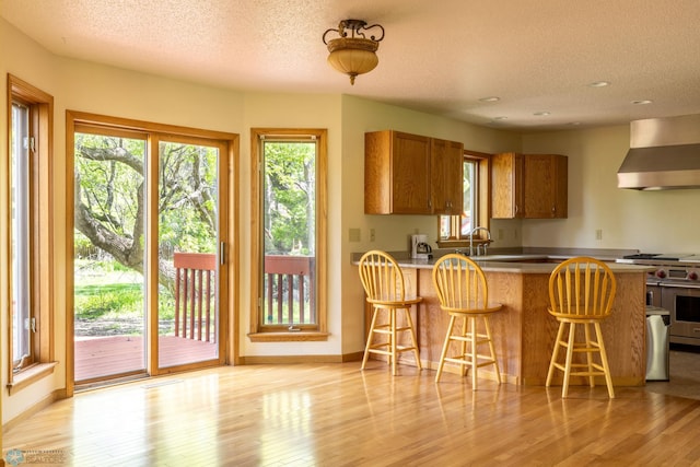 kitchen featuring a kitchen breakfast bar, wall chimney exhaust hood, light wood-type flooring, and range with two ovens