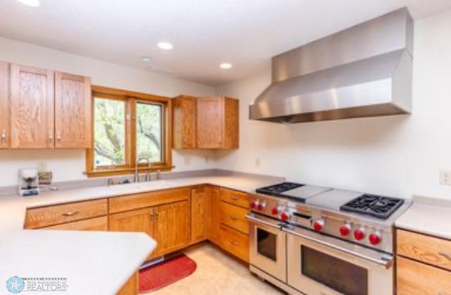 kitchen featuring wall chimney range hood, sink, and range with two ovens