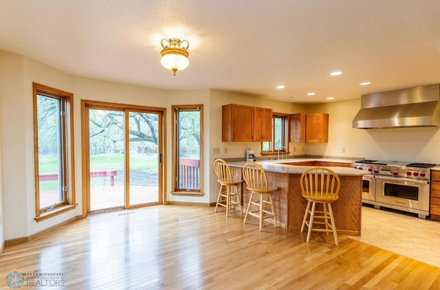 kitchen with double oven range, a wealth of natural light, a breakfast bar, and wall chimney exhaust hood