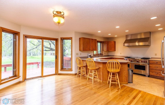 kitchen featuring light hardwood / wood-style floors, kitchen peninsula, a breakfast bar area, wall chimney exhaust hood, and double oven range