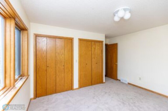 unfurnished bedroom featuring multiple closets and carpet flooring