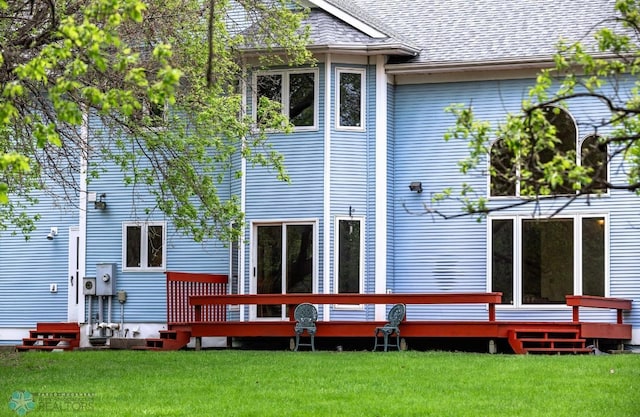 rear view of property featuring a wooden deck and a lawn