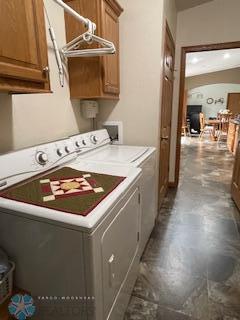 clothes washing area with dark tile flooring, washing machine and clothes dryer, and cabinets