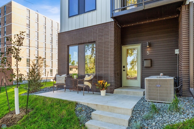 entrance to property with a balcony, cooling unit, a patio area, and a yard