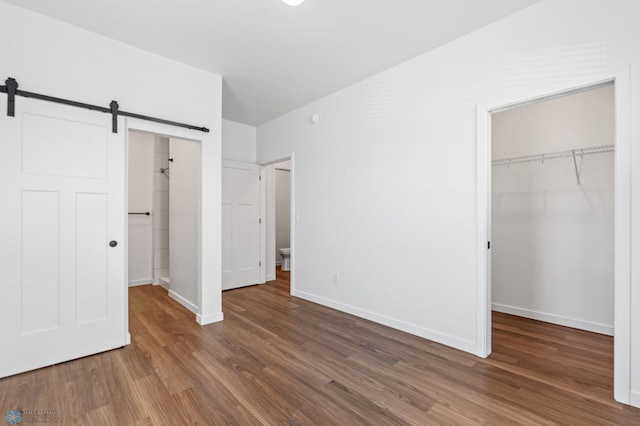 unfurnished bedroom with dark hardwood / wood-style flooring, a closet, and a barn door