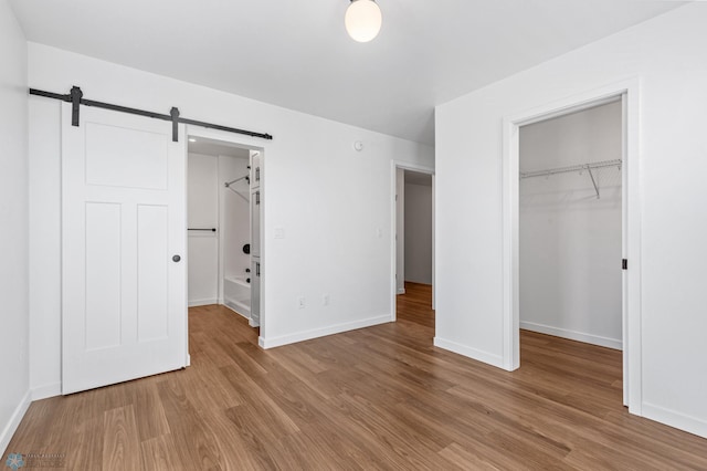 unfurnished bedroom featuring a closet, light hardwood / wood-style flooring, a barn door, and a spacious closet