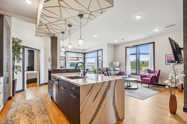 kitchen featuring a center island with sink, stainless steel dishwasher, sink, and light wood-type flooring