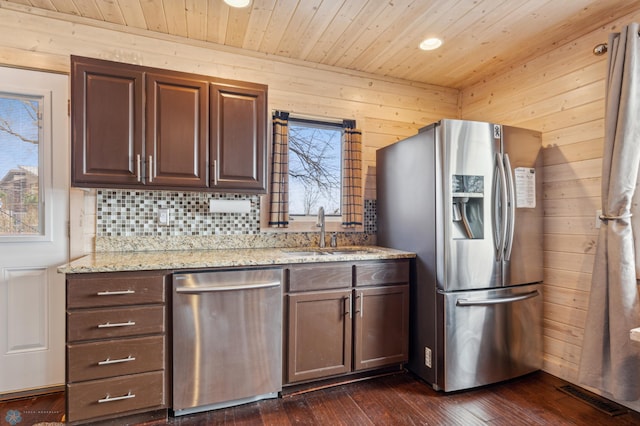 kitchen featuring light stone countertops, dark wood-type flooring, wooden walls, sink, and appliances with stainless steel finishes