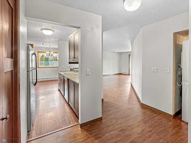 corridor with an inviting chandelier, a textured ceiling, a baseboard heating unit, hardwood / wood-style flooring, and sink