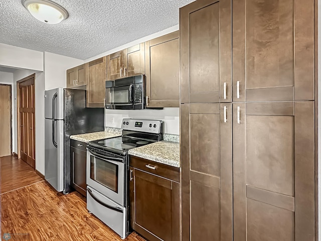 kitchen with light stone counters, dark brown cabinets, light hardwood / wood-style floors, a textured ceiling, and electric range