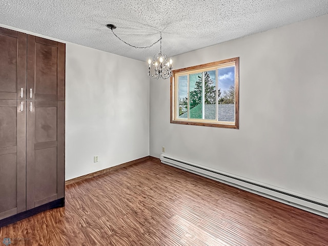 unfurnished dining area featuring an inviting chandelier, baseboard heating, a textured ceiling, and hardwood / wood-style floors