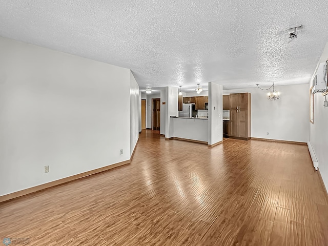 unfurnished living room featuring a notable chandelier, baseboard heating, a textured ceiling, and hardwood / wood-style floors