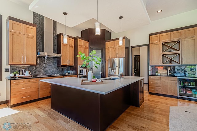 kitchen featuring beverage cooler, a kitchen island with sink, backsplash, and wall chimney exhaust hood