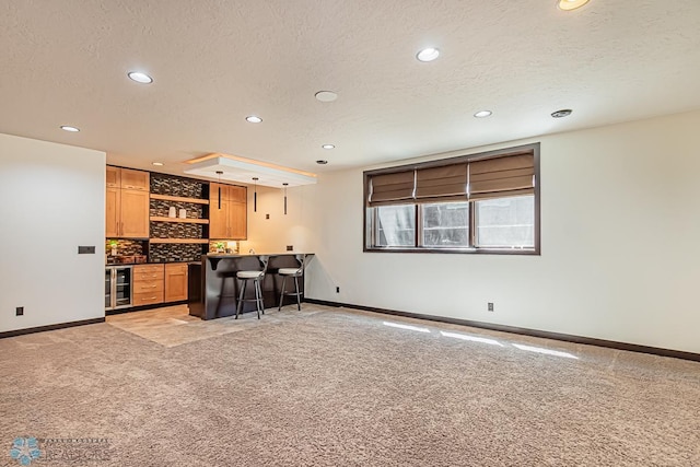 kitchen featuring a textured ceiling, wine cooler, a kitchen bar, and light colored carpet