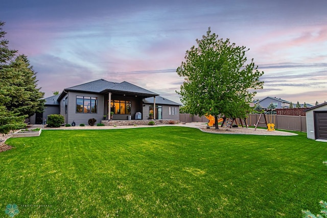 back house at dusk featuring a patio and a lawn