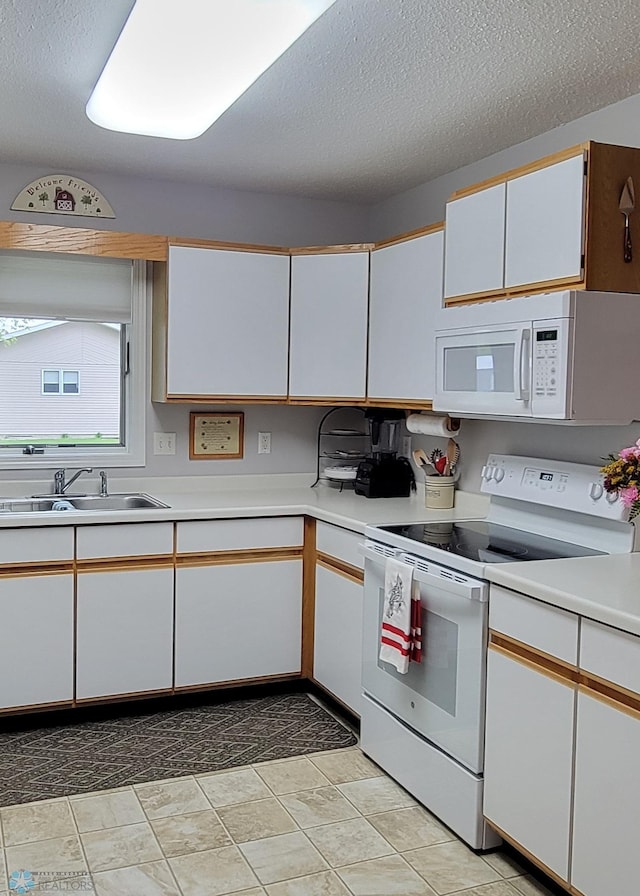 kitchen with white appliances, light tile flooring, a textured ceiling, sink, and white cabinetry