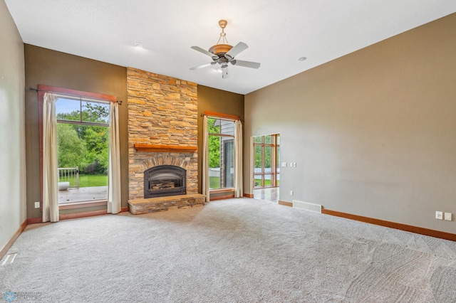 unfurnished living room featuring a stone fireplace, carpet floors, and ceiling fan