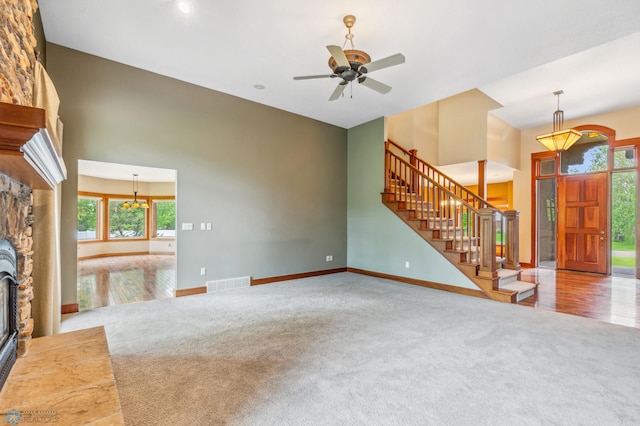 living room with a stone fireplace, a high ceiling, ceiling fan, and carpet floors