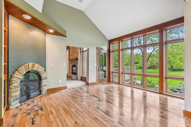 unfurnished living room featuring a healthy amount of sunlight, wood-type flooring, a stone fireplace, and high vaulted ceiling