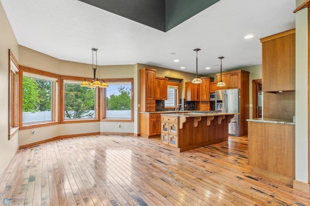 kitchen with a kitchen island, decorative light fixtures, stainless steel appliances, and light wood-type flooring