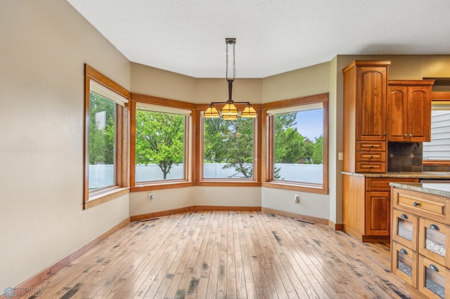 unfurnished dining area featuring a notable chandelier, a wealth of natural light, and light hardwood / wood-style flooring