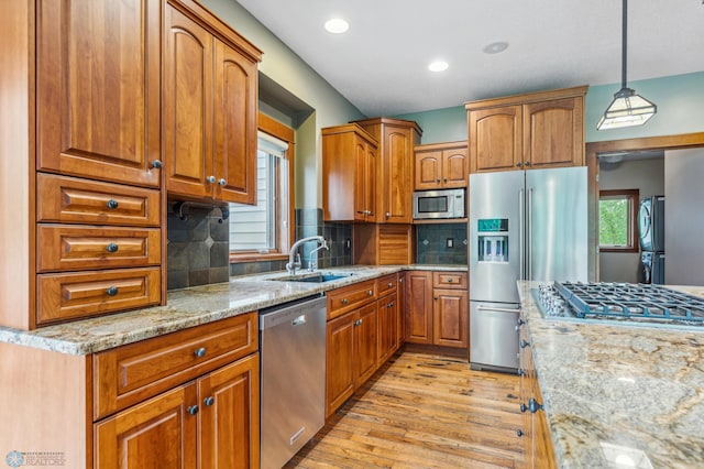 kitchen with stainless steel appliances, backsplash, hanging light fixtures, light wood-type flooring, and sink