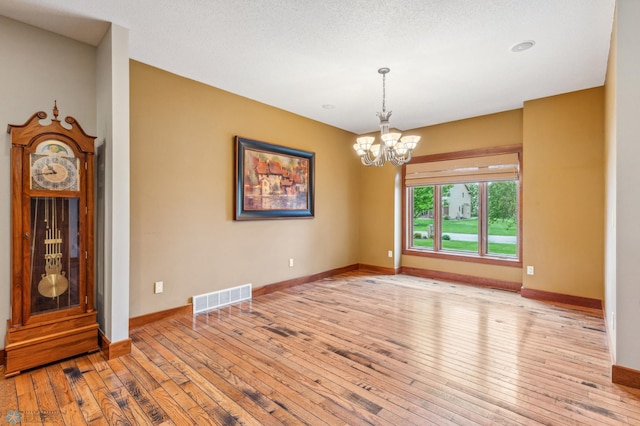 empty room featuring a textured ceiling, light wood-type flooring, and a chandelier