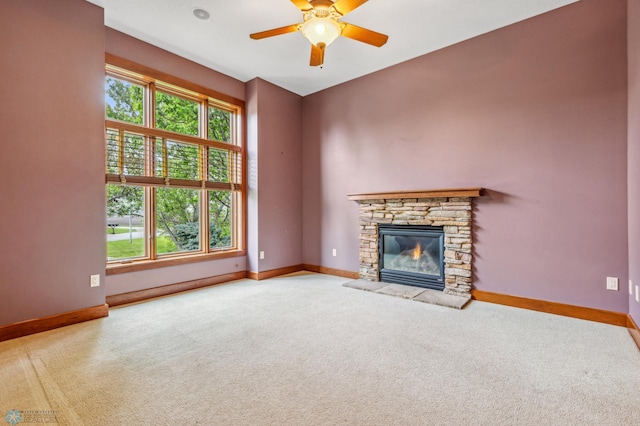 unfurnished living room featuring a stone fireplace, carpet, and ceiling fan