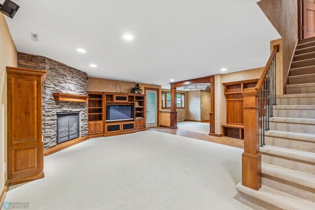 unfurnished living room featuring a baseboard heating unit, a stone fireplace, and light carpet