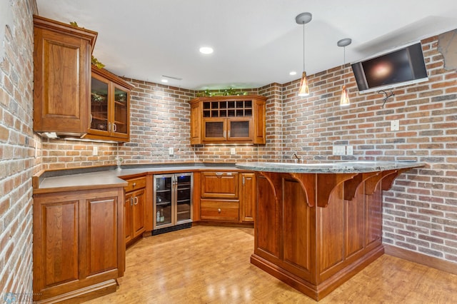 kitchen featuring beverage cooler, light hardwood / wood-style floors, decorative light fixtures, brick wall, and a kitchen bar