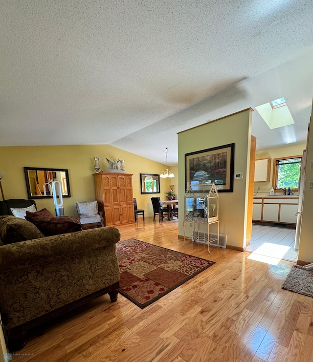 living room featuring sink, a textured ceiling, light hardwood / wood-style flooring, a chandelier, and lofted ceiling with skylight