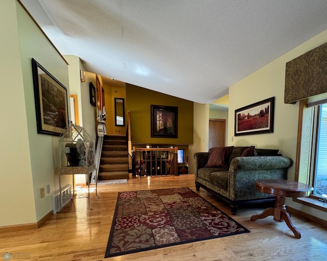 living room with a textured ceiling, light wood-type flooring, lofted ceiling, and a healthy amount of sunlight