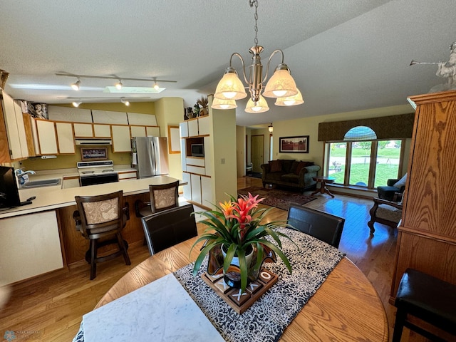 dining space featuring an inviting chandelier, sink, light hardwood / wood-style floors, and a textured ceiling