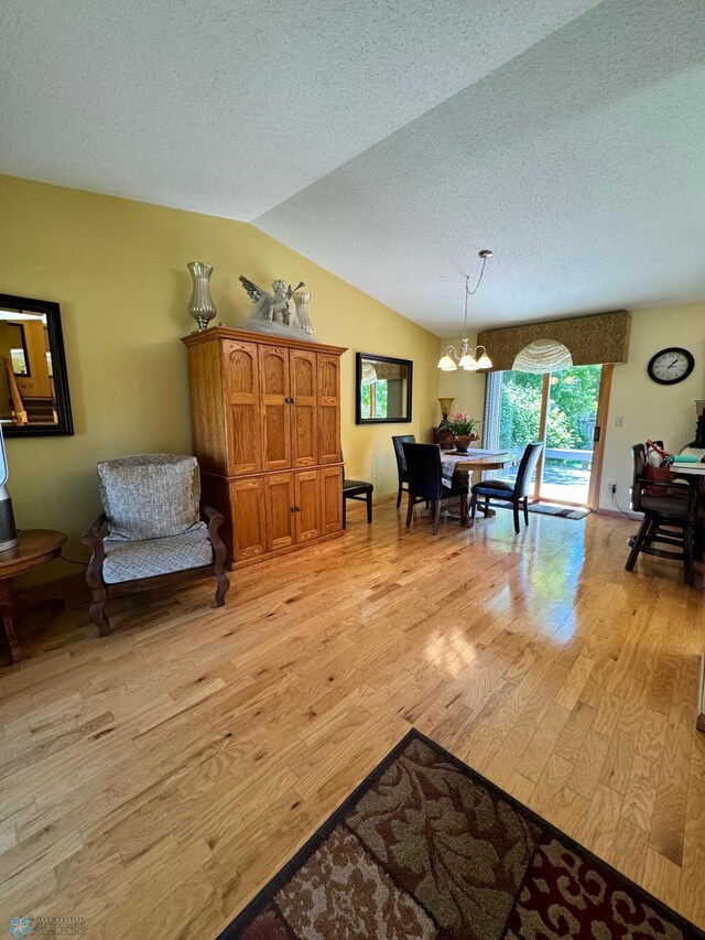 interior space with a notable chandelier, light hardwood / wood-style flooring, vaulted ceiling, and a textured ceiling