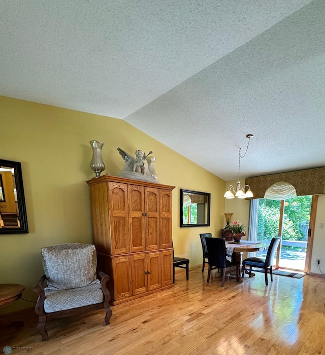 dining space with a textured ceiling, lofted ceiling, a notable chandelier, and light hardwood / wood-style flooring