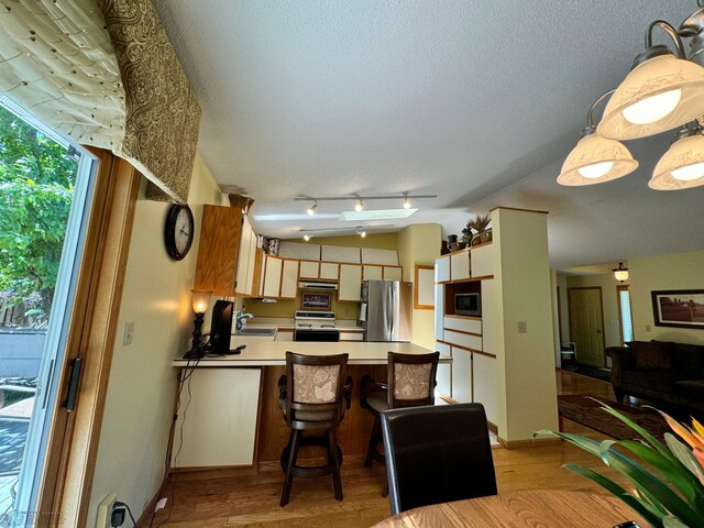 kitchen featuring light wood-type flooring, exhaust hood, sink, kitchen peninsula, and appliances with stainless steel finishes