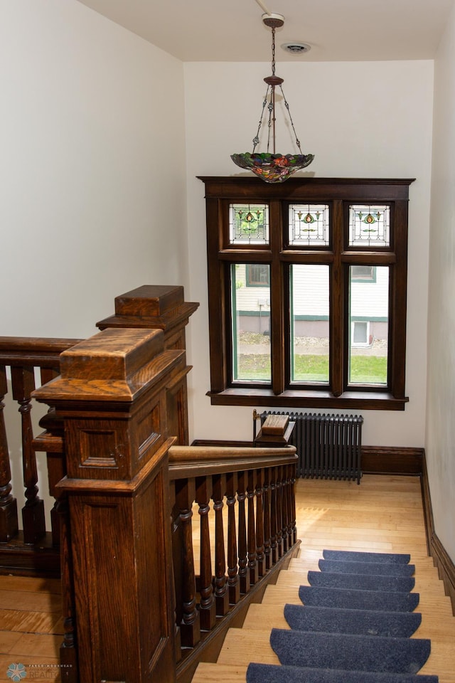 staircase featuring radiator heating unit, a healthy amount of sunlight, and light wood-type flooring