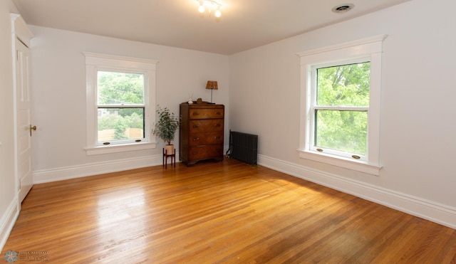 empty room with plenty of natural light, light hardwood / wood-style floors, and radiator