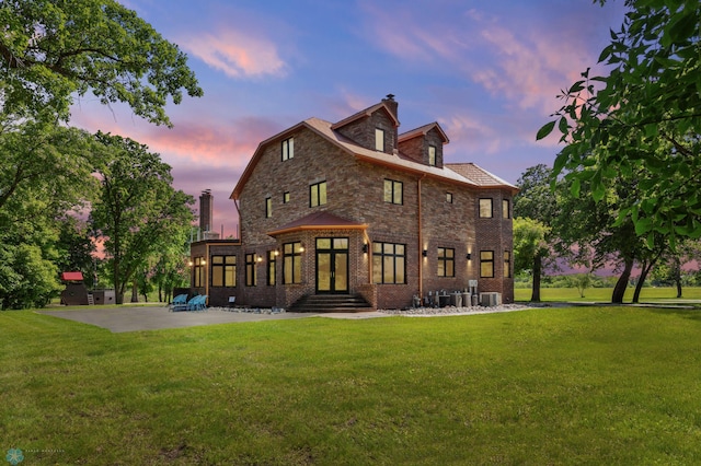 back house at dusk featuring a lawn, central AC unit, and a patio