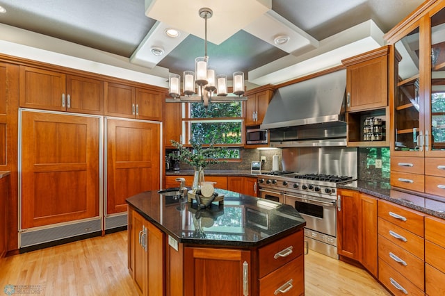 kitchen featuring a center island, wall chimney range hood, light hardwood / wood-style flooring, built in appliances, and tasteful backsplash