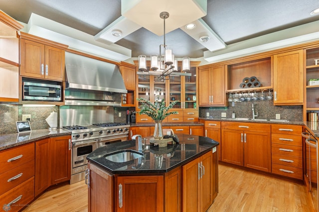 kitchen with wall chimney range hood, an island with sink, light hardwood / wood-style flooring, and tasteful backsplash