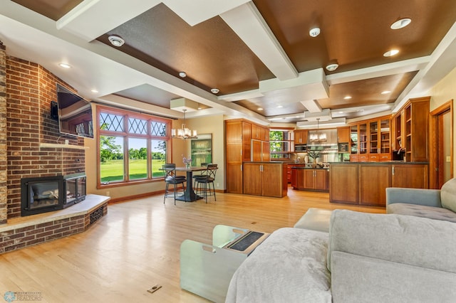 living room featuring a wealth of natural light, an inviting chandelier, light wood-type flooring, and a brick fireplace