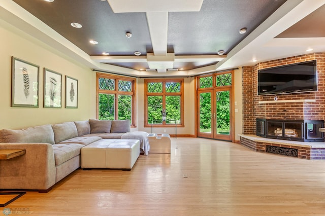 living room with a tray ceiling, a wealth of natural light, a brick fireplace, and light hardwood / wood-style flooring