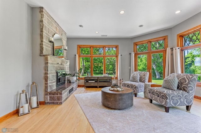 living room with a stone fireplace, light hardwood / wood-style floors, and french doors