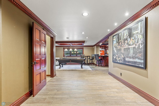 corridor with a tray ceiling, ornamental molding, and light wood-type flooring